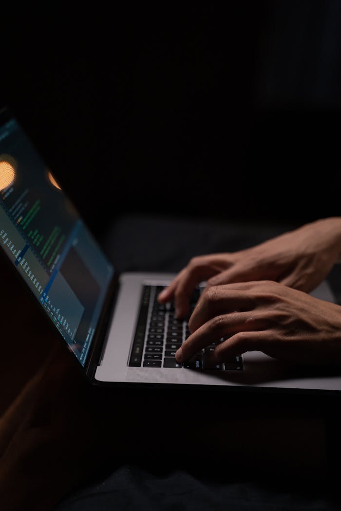 The Art of Drawing Readers In: Your attractive post title goes here Hands typing code on a laptop keyboard in a dark room, capturing the essence of late-night programming.